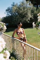 Aura - Bikini in Plum / Pink Polka Dot — full front view reading by the garden railing